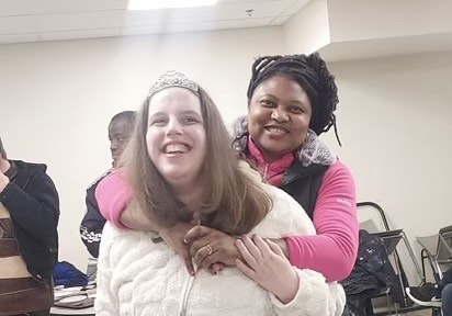 A staff member hugs an adult resident, both are smiling at the camera.