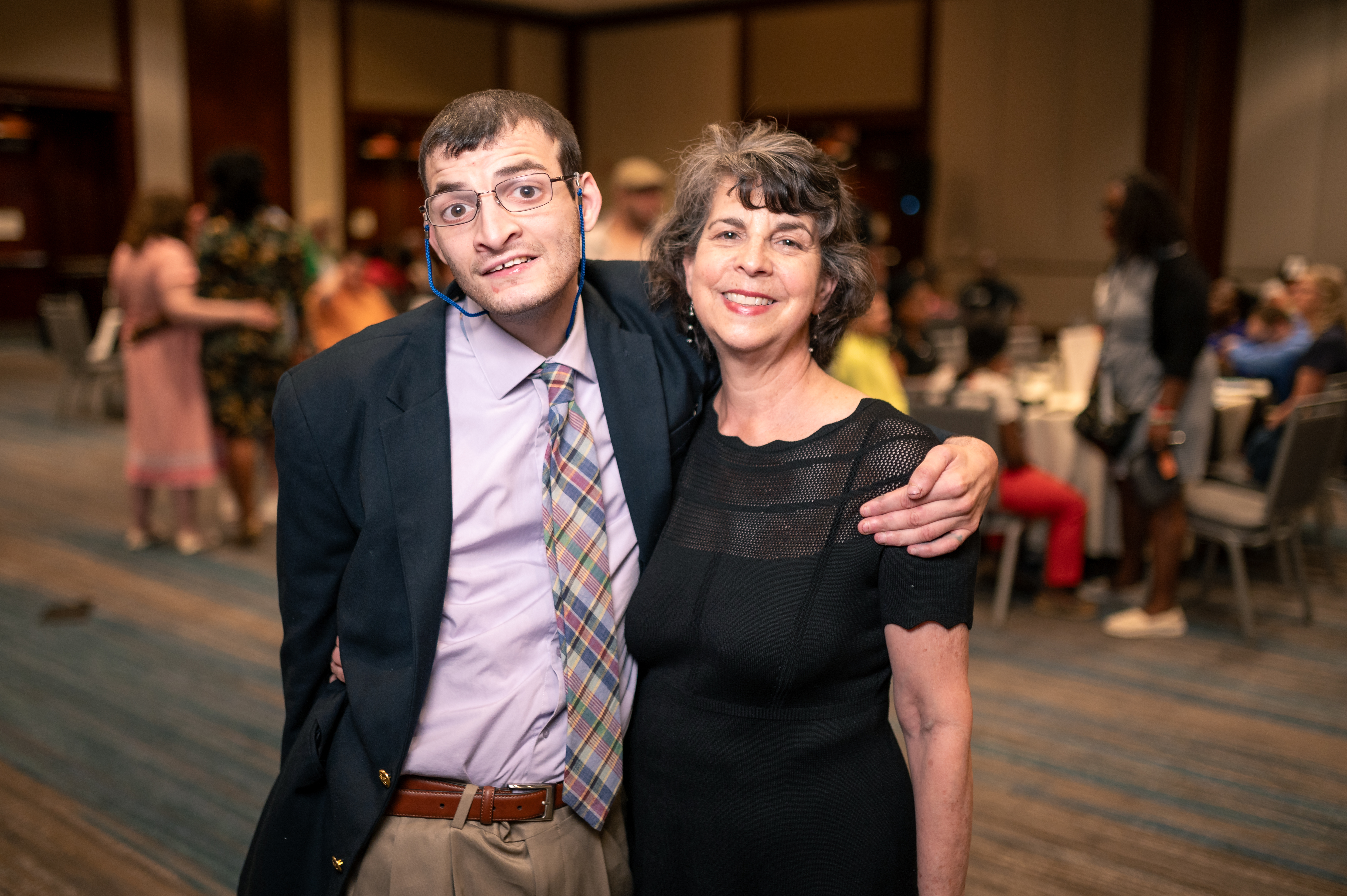 A mother and son stand together with their arms around each other at a formal event.