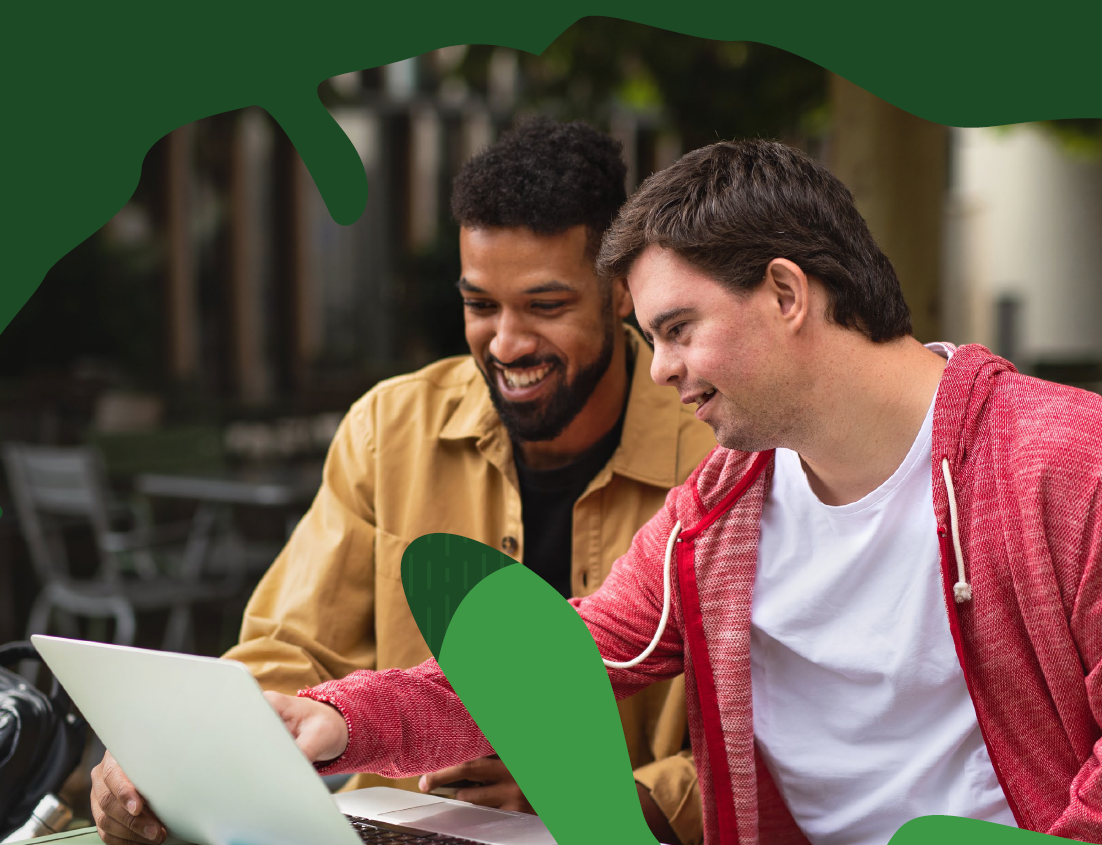 Two men are working closely together on a laptop and smiling.