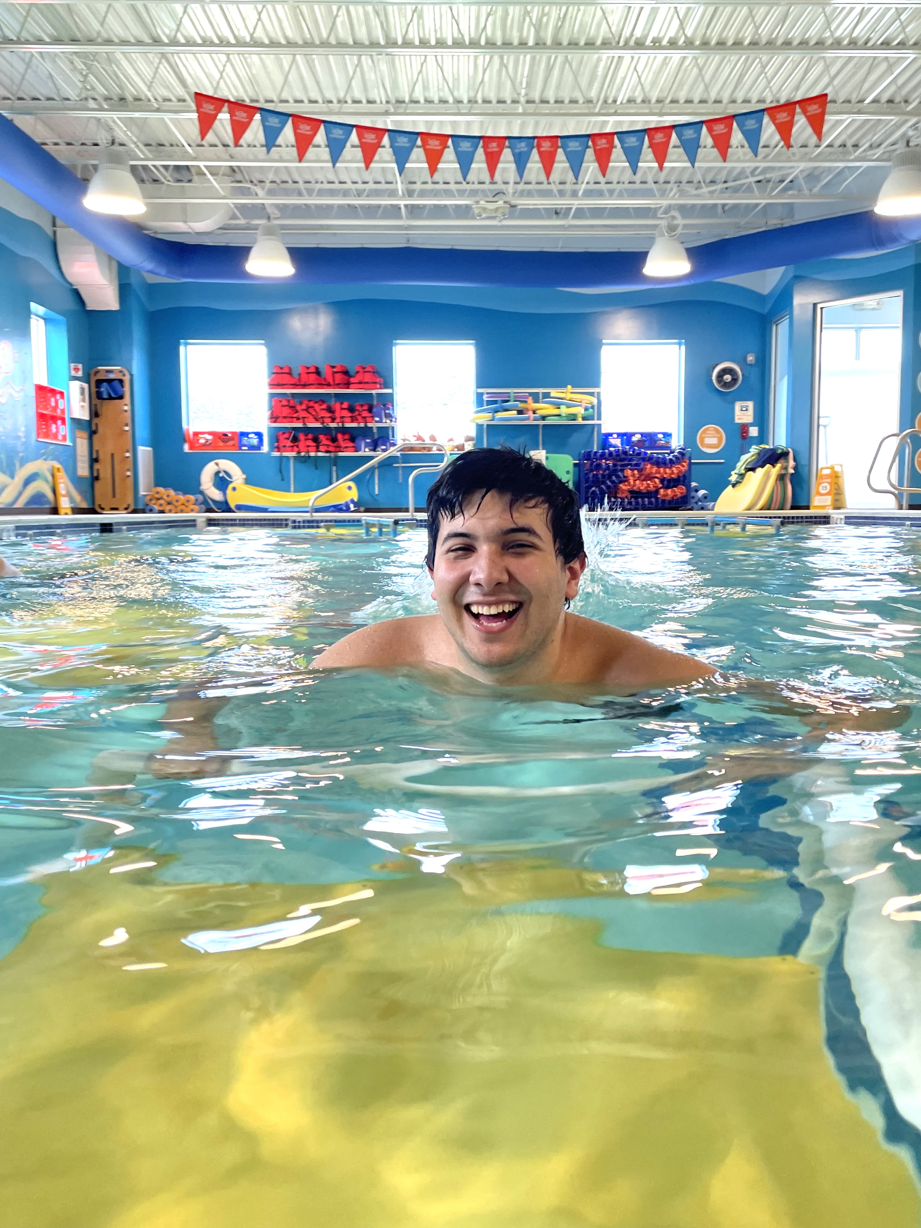 A student smiles as he swims in a pool.