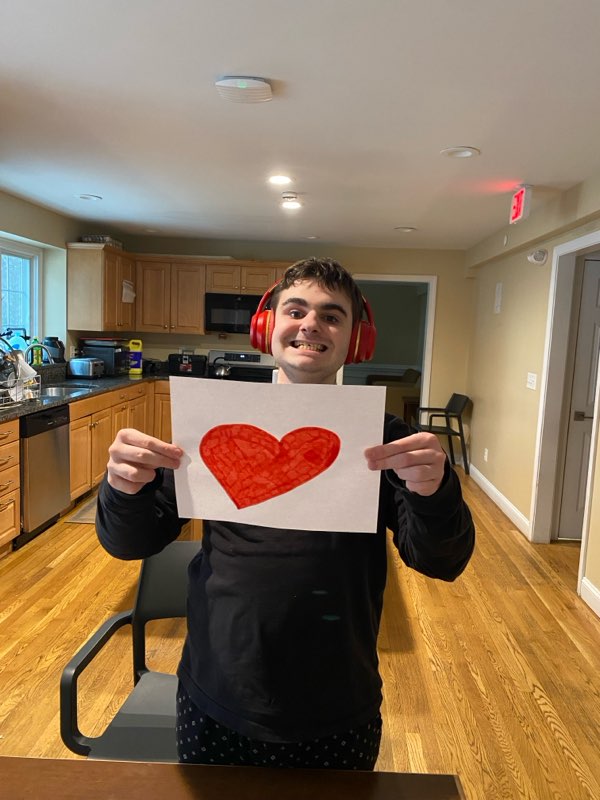 A student holds up a hand-drawn illustration of a red heart.