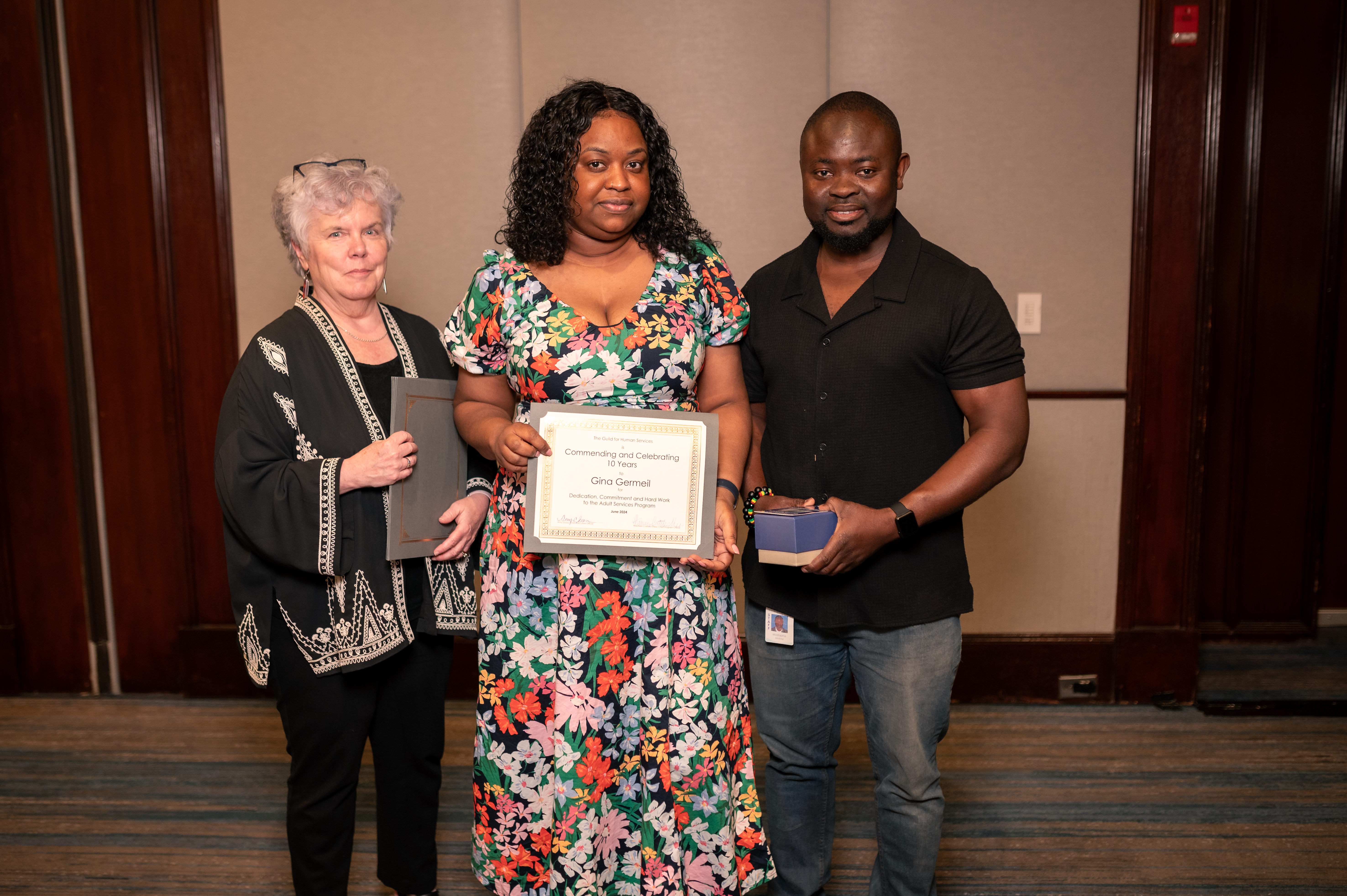 Three staff members pose for a photo with an award recognizing Gina Germeil (center) for 10 years of service in the adult residential program.