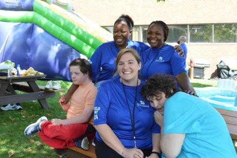 Two students and three staff sit close together on a picnic table outside at The Guild School Field Day.