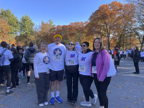 A group of fundraisers and staff pose together at a busy 5K event, wearing matching Guild shirts