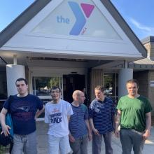 A group of 5 male residents stand together in front of the YMCA building in their community.