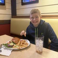 A student smiles with his meal at a restaurant table.